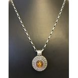 An unusual round silver decorative locket set with a central amber cabochon on 18 inch chain.