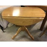 A small light wood drop leaf kitchen table with pedestal base.