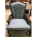 A dark wood framed armchair with cane backing and blue button back upholstery.