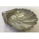 An ornate silver clam shaped dish with floral decoration and 3 conch shaped feet.