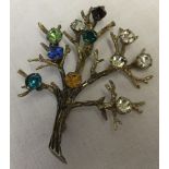 A sterling silver brooch in the shape of a tree set with coloured stones in the branches.