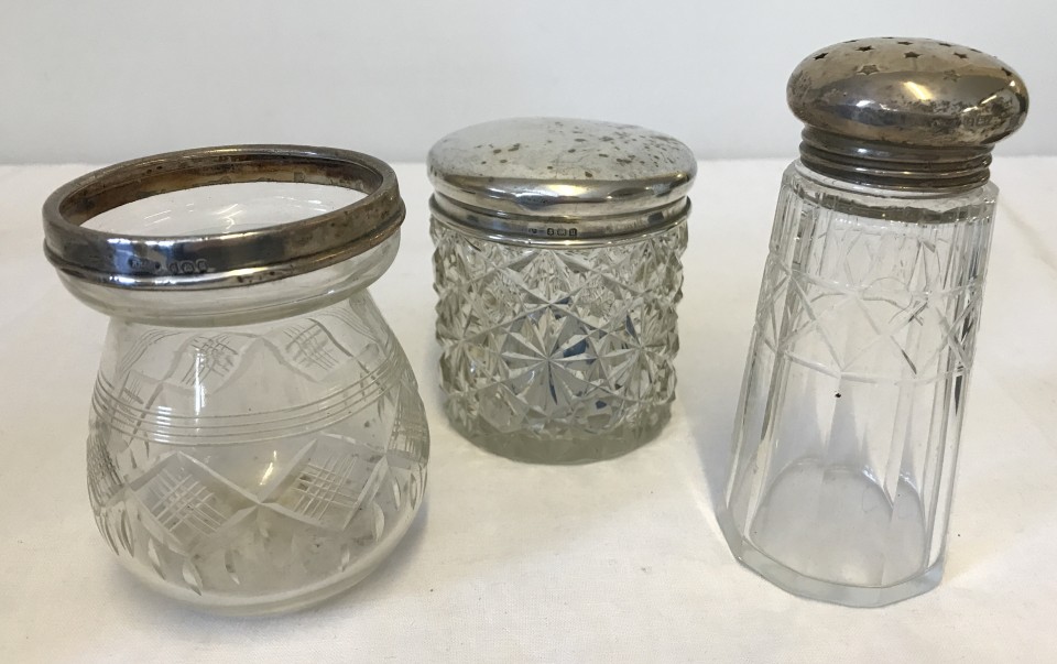 A silver lidded jar together with a silver topped sugar sifter and silver rimmed preserve pot.