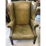 A vintage wing back chair with dark wood legs and olive green studded leather upholstery.