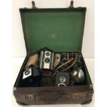 A collection of vintage cameras, accessories and binoculars in a small vintage suitcase.