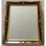 A modern reproduction ornate framed wall hanging mirror with bevel edged glass and gilt decoration.