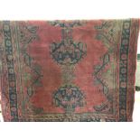A large wool rug of red, blue and green with floral decoration to edges.