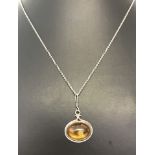 An oval amber pendant in a silver mount on a silver chain.