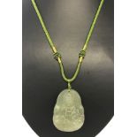 Carved jade Buddha pendant hanging on green cord.