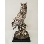 A silver painted resin owl on a stump figure on wooden plinth.