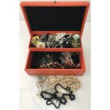 A vintage orange jewellery box containing a quantity of vintage jewellery.