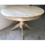 A modern circular pine kitchen table with pedestal base.