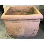 A large square shaped terracotta garden planter with fern decoration to corners and sides.