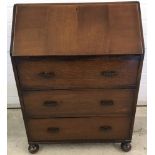 A vintage dark oak bureau with ball feet to front and stationery compartments.