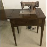 A 1960's dark wood 185k Singer electric sewing machine table with accessories, lamp and foot pedal.