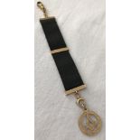 A 9ct gold Masonic fob mounted on a black ribbon clip.