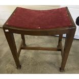 A vintage curve topped wooden stool with tapered legs and red velvet upholstery seat.