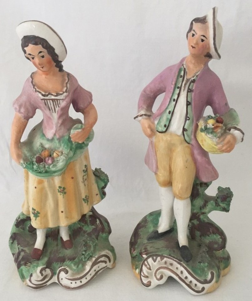 A pair of Victorian ceramic figurines of a man and woman holding baskets of fruit.