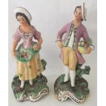 A pair of Victorian ceramic figurines of a man and woman holding baskets of fruit.