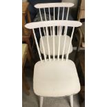 A pair of vintage wooden stick back kitchen chairs painted white.