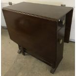 A vintage dark wood drop leaf gate leg table with cupboards to ends.