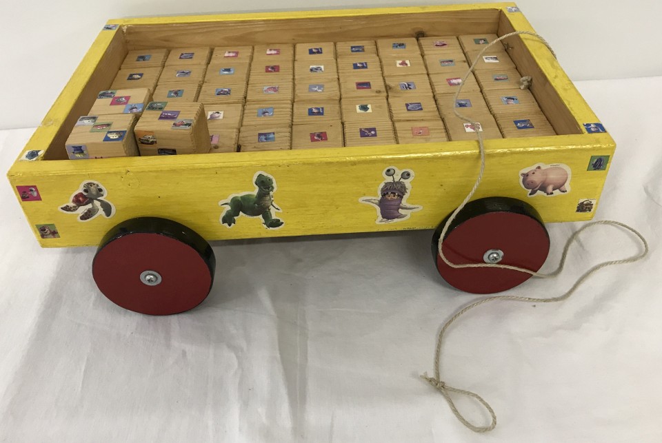 A wooden pull along child's trolley filled with wooden blocks decorated with Disney stickers.