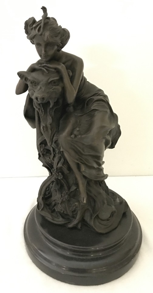 A bronze of a woman draped over a wolf's head statue.