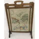 A vintage oak fire screen with needlework panel behind glass.