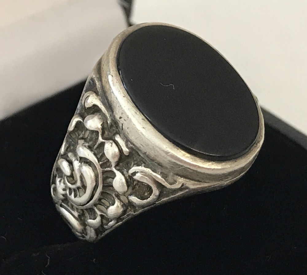 A men's silver and onyx signet ring with decorative detail to shoulders.