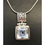 A silver and square cut topaz pendant on a silver rope chain.