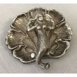 A silver brooch in the shape of a mermaid sitting in a shell.