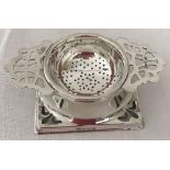 A hallmarked silver tea strainer and stand with pierced work detail to handles and corners of stand.