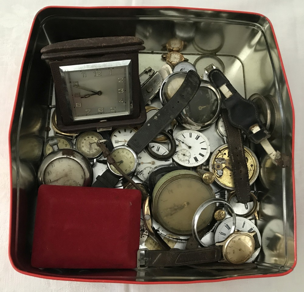 A tin of mixed wristwatch and pocket watch parts and spares together with a cased travel clock.