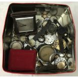 A tin of mixed wristwatch and pocket watch parts and spares together with a cased travel clock.