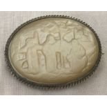 A vintage metal brooch set with carved mother of pearl depicting an oriental scene.
