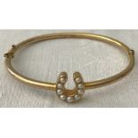 A gold hinged bangle with horseshoe set with seed pearls.