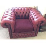 A vintage red leather Chesterfield chair with upholstered seat cushion.