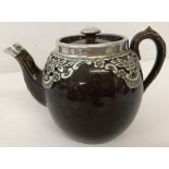 A ceramic teapot brown glaze teapot with silver clad rim and silver floral decoration to body.