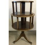 A 2 tier circular revolving book stand on pedestal base with tripod legs and brass castor feet.
