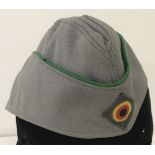 German post WWII overseas side cap in field grey fabric with green piping.