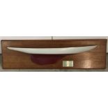 A wall hanging yacht half hull mounted on wooden plaque.