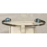 A 9ct white gold bangle set with 2 oval cut blue topaz stones.