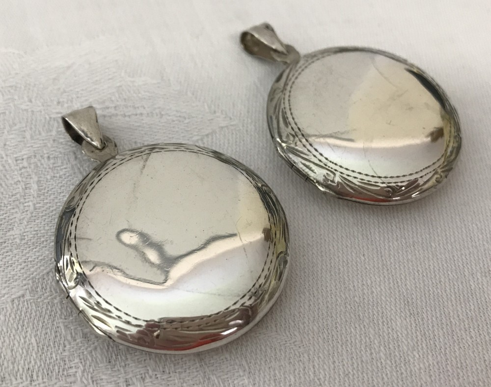 2 large round silver lockets with engraving to outer edge.