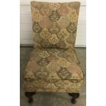 A vintage nursing chair with front cabriole style legs and upholstery in neutral tones.