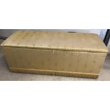A vintage ottoman with gold fabric cover and fringe bottom.