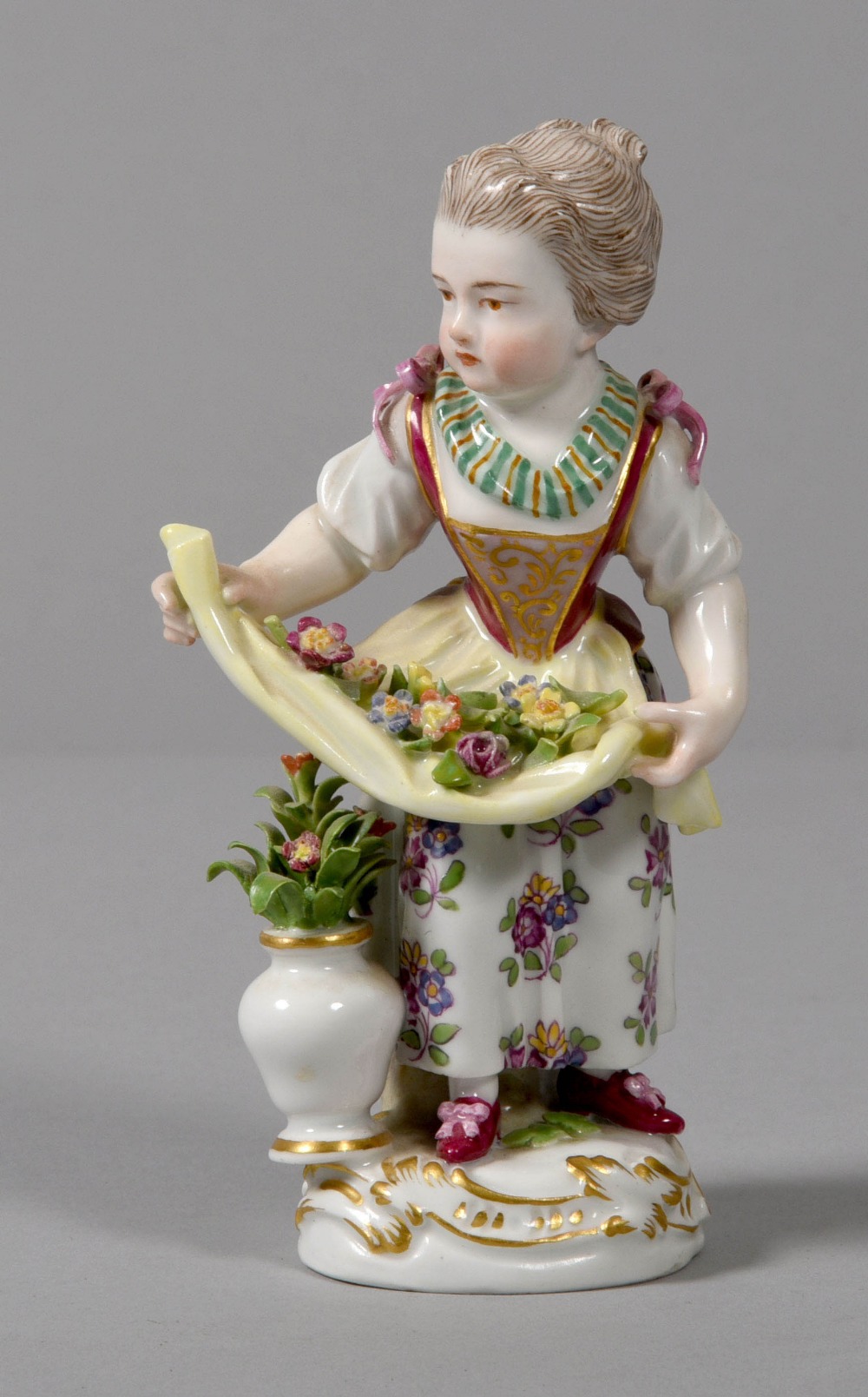 A Meissen porcelain figurine of a girl with flowers and apron with floral dress and a vase of