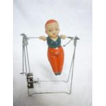 A Celluloid and metal clockwork toy depicting a gymnast on a bar apparatus