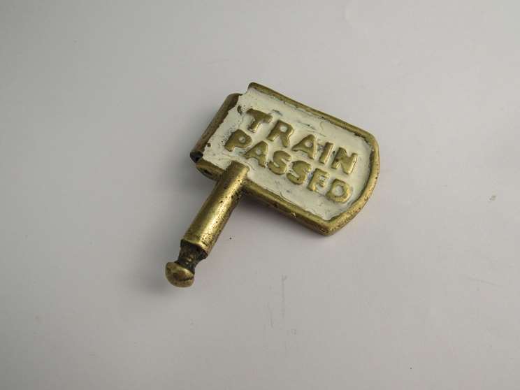 A brass single line key token with "TRAIN ON LINE" and "TRAIN PASSED" on each sides