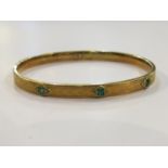 A child's gold bangle set with three square cut emeralds, engraved 'chevron decoration',