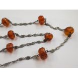 An opera length white metal link chain necklace interspersed with facet cut amber beads