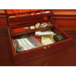 A red jewellery box containing costume jewellery including pocket watch, earrings,